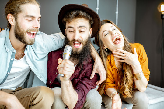 Young And Cheerful Friends Singing With Microphone While Playing Karaoke At Home