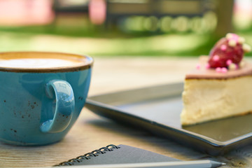 Latte coffee, cheesecake and notebook on the table
