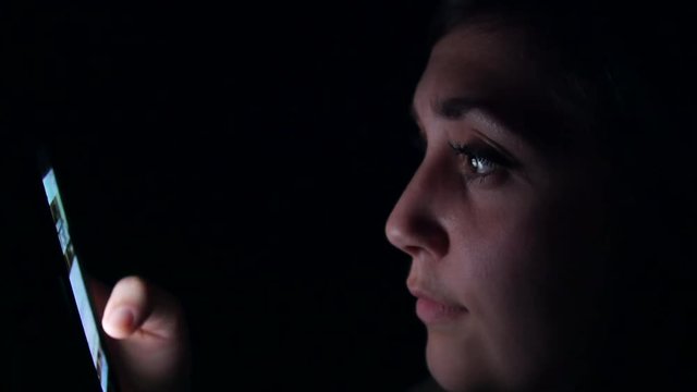 Woman scrolls through her social media feed on her smart phone late at night.