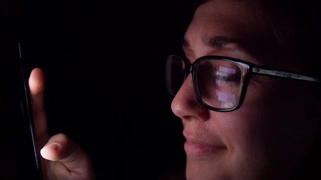 Smiling woman scrolls through social media feed late at night.