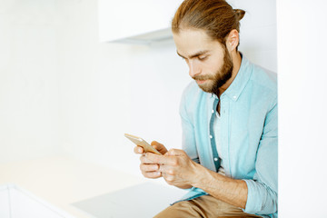 Handsome man using phone while sitting on the white kitchen at home