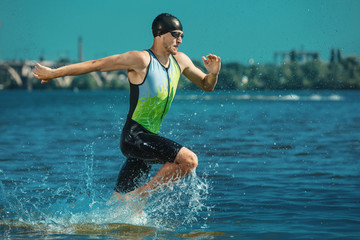 Professional triathlete swimming in river's open water. Man wearing swim equipment practicing triathlon on the beach in summer's day. Concept of healthy lifestyle, sport, action, motion and movement.