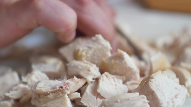 Close up, selective focus on male hands with finger tattoo, chopping & dicing fresh, cooked chicken pieces for healthy, nutritious meal.
