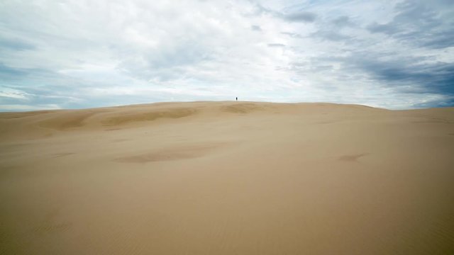 Cinematic Shot of Desert Dune With Person in Distance on Top Of Sand Hill Under Beautiful Cloudy Skyline 4k