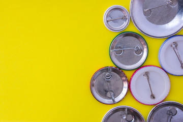 Inverted metal badges with clasps on yellow uniform background view from above with the clear area of half photo for labels, headers. Concept photo for prizes, souvenirs