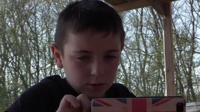 cute young boy sitting outside, playing on his smartphone