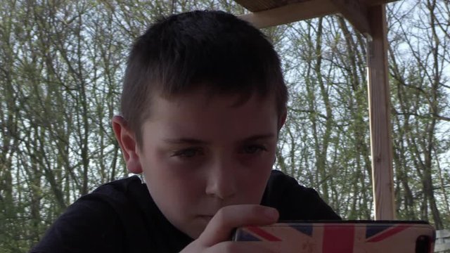 young boy concentrated on his smartphone while sitting outside on a sunny day