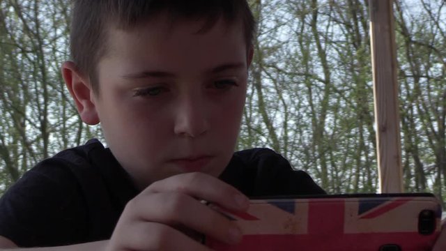 young boy sitting outside, enjoying his smartphone, playing games, SLO-MO