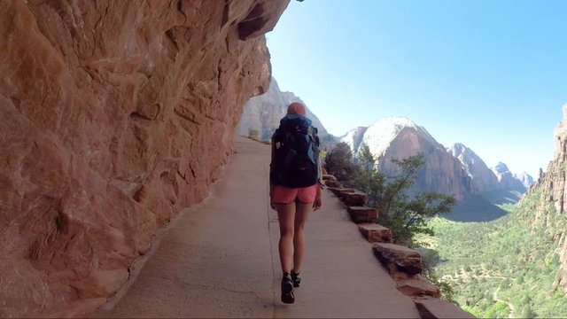 Young woman wearing backpack is walking to Angel's Landing in Zion National park in Utah, USA. Female on a hiking trail in Zion National Park in Usa
