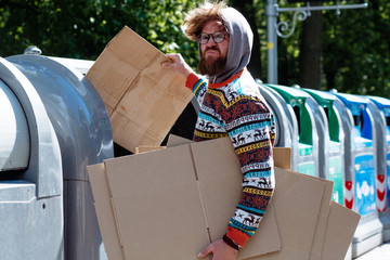 Homeless man collecting waste paper. Stylish beggar taking carton boxes from container for waste paper in the trash cans in the city street. Concept of poor life poverty unemployment