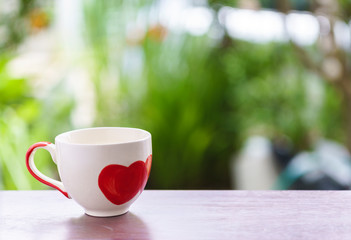Cup of coffee with red heart on blur green background