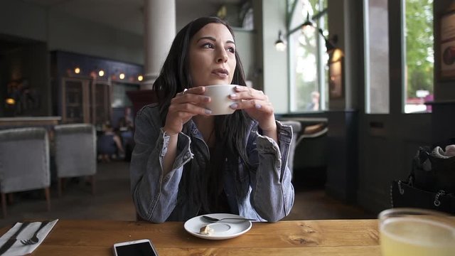 Attractive latina brunette sitting at the table having a coffee, waiting, thinking and looking outside