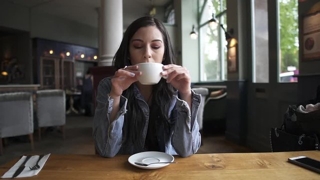 Hispanic latina brunette sitting at the table having a coffee, waiting, thinking and looking outside