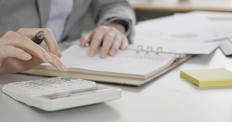 female businesswoman in suit hand using calculator plan to write and sign check book with graph data paper on desk at office. Paycheck concept. secretary assistant accounting financial in company