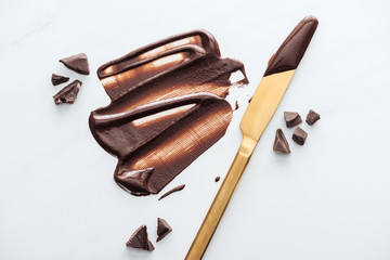 Top view of gold table knife with liquid chocolate and pieces of chocolate