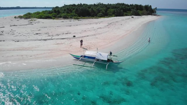 Wooden asian tourist boat with tourists on a white sand beach in Balabac, Palawan, drone shot in Patawan Island, Philippines