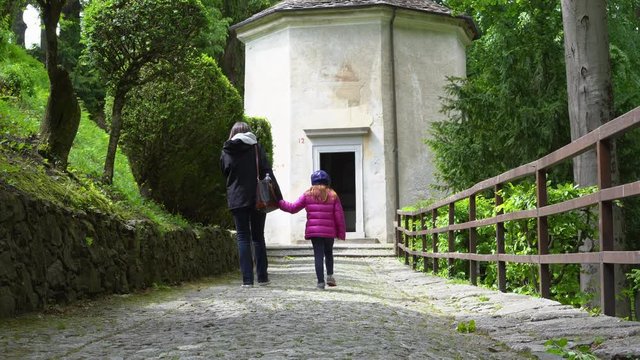 A mother and her little daughter carrying a teddy bear visiting the sacred mountain of Varallo christian devotional complex, a unesco world heritage site near the town of Varallo Sesia in Italy