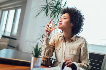 Young beautiful african american woman relaxing and listening to music using headphone, drinking wine.