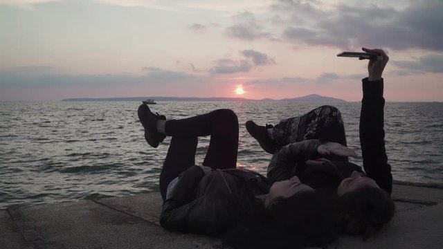 Two girls are taking selfie of themselves near the sea at the sunset