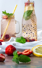 A glass bottle and a jar with refreshing strawberry, lemon and mint shakes on a white background and a white towel