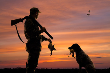 hunter and his dog with downed duck at sunset