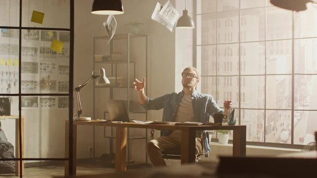 Frustrated and Tired Young Creative Designer Works on Laptop at His Desk, He Browses Through Concept Sketches. Feeling Anger and Dissatisfaction He Throws Sheets into the Air out of Sheer Despair