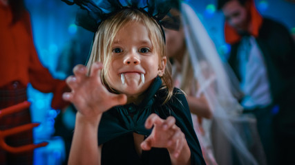 Halloween Costume Party: Cute Little Bat Girl with Sharp Fangs Makes Scary Funny Faces. In the...