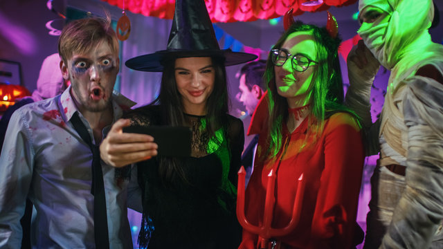 Halloween Costume Party: Brain Dead Zombie, Blood Thirsty Dracula, Bandaged Mummy Beautiful Witch and Seductive She Devil Posing for Group Video Selfie Taken with Smartphone. Monsters Have Fun.