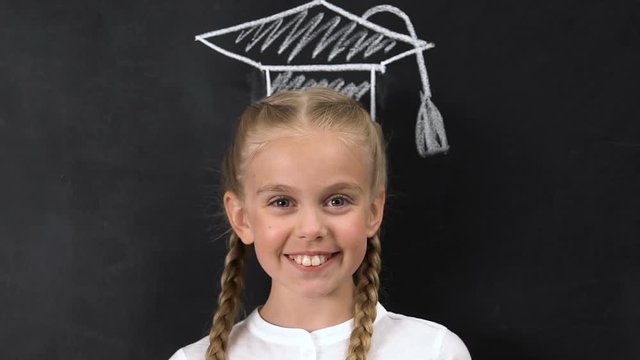 Schoolgirl with square academic cap painted above head smiling at camera