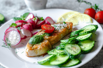 Salmon steak with lemon, tomatoes, cucumber and radish on a plate. Healthy seafood. Proper nutrition food.
