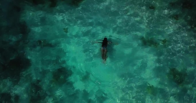 Top down aerial view, showing a girl diving in stunning crystal clear blue water.