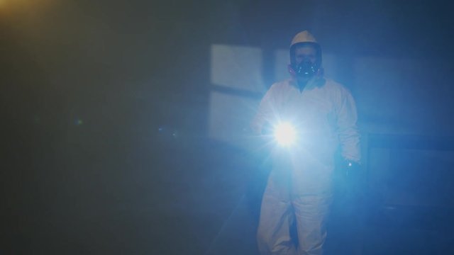 Hazmat suit wearing man explores a dark room
