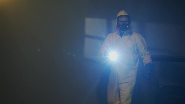 Hazmat suit wearing man explores a dark room