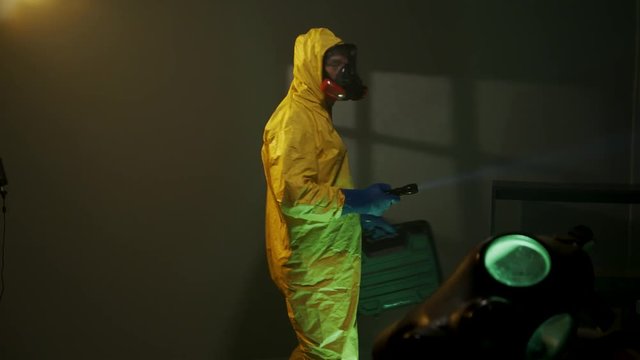 Hazmat suit wearing man explores a dark room