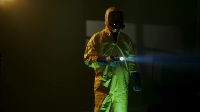 Hazmat suit wearing man explores a dark room