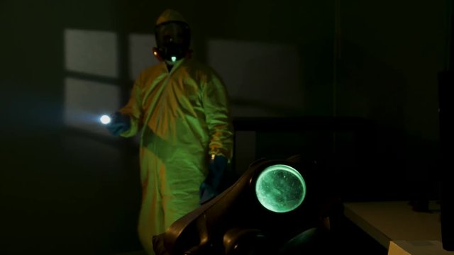 Hazmat suit wearing man explores a dark room