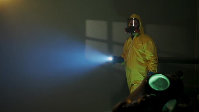 Hazmat suit wearing man explores a dark room