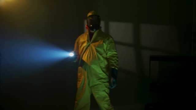 Hazmat suit wearing man explores a dark room
