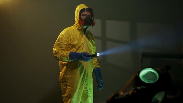 Hazmat suit wearing man explores a dark room