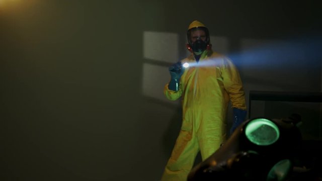 Hazmat suit wearing man explores a dark room