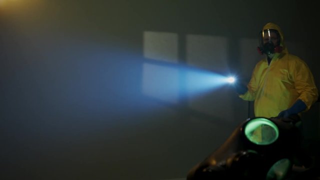 Hazmat suit wearing man explores a dark room