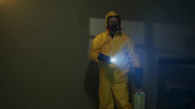 Hazmat suit wearing man explores a dark room