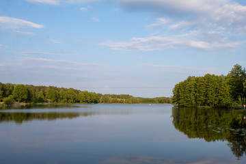 Fototapeta premium Landscape of a beautiful superficial blue lake surrounded by forest in the central part of Poland on a sunny summer day.