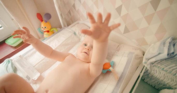 Baby girl stretches out hands on the changing mat, wants to get up