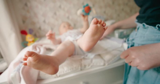 Mother changing the diaper of her baby girl at home on a baby changing table