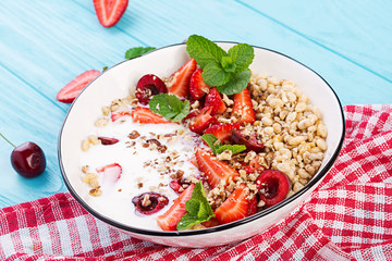 Healthy breakfast - granola, strawberries, cherry, nuts and yogurt in a bowl on a wooden table. Vegetarian concept food.