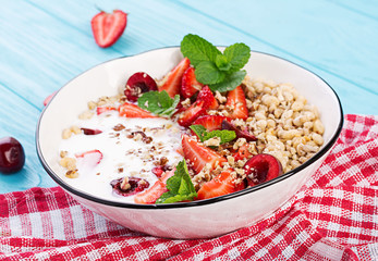Healthy breakfast - granola, strawberries, cherry, nuts and yogurt in a bowl on a wooden table. Vegetarian concept food.