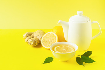Ginger lemon tea or detox drink in a white cup and a teapot on a bright yellow background. Healthy eating concept.