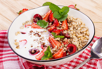 Healthy breakfast - granola, strawberries, cherry, nuts and yogurt in a bowl on a wooden table. Vegetarian concept food.