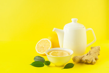 Ginger lemon tea or detox drink in a white cup and a teapot on a bright yellow background. Healthy eating concept.